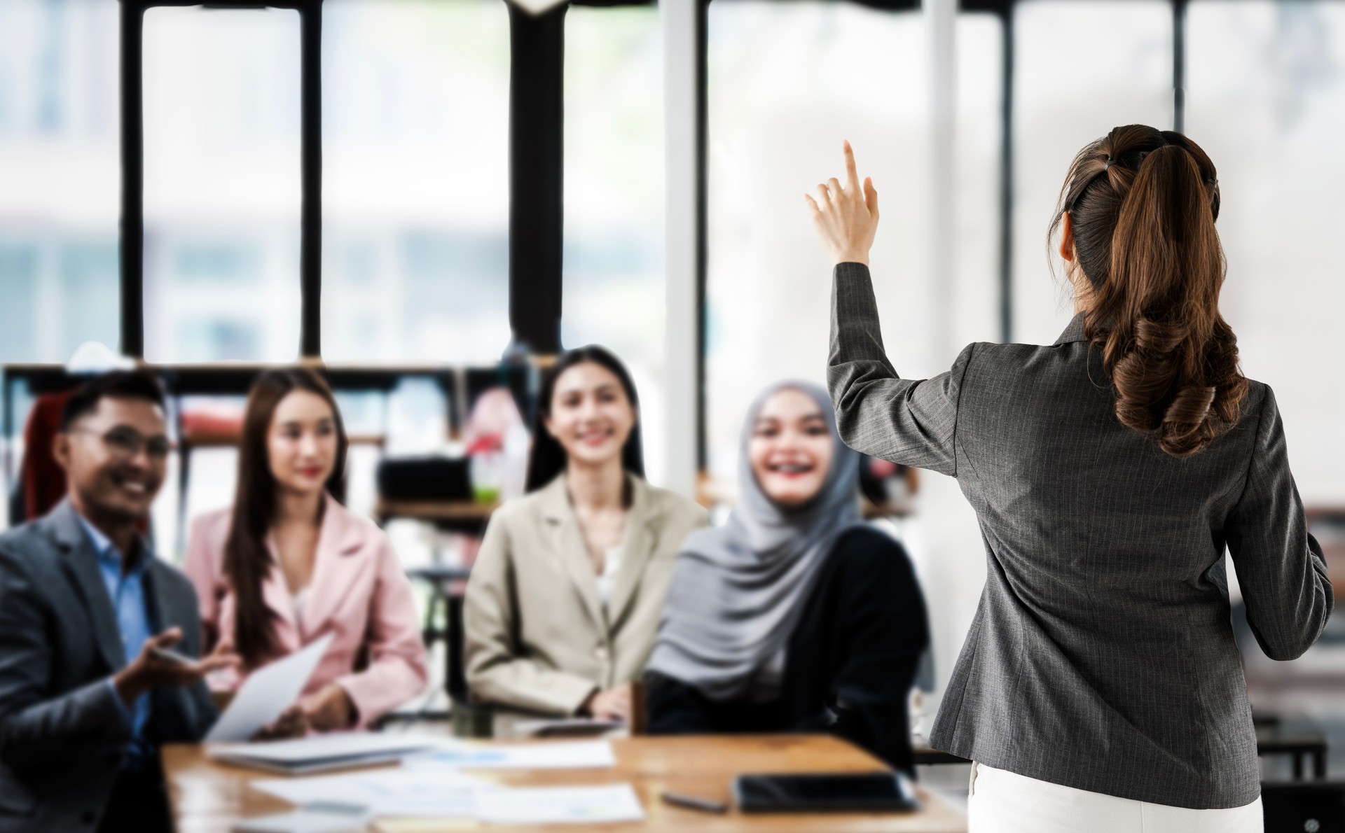 Rear view of Business woman briefing and presenting standing in meeting room with colleague, training for company project, collaboration meeting and discussion, presenter and coworkers for work strategy