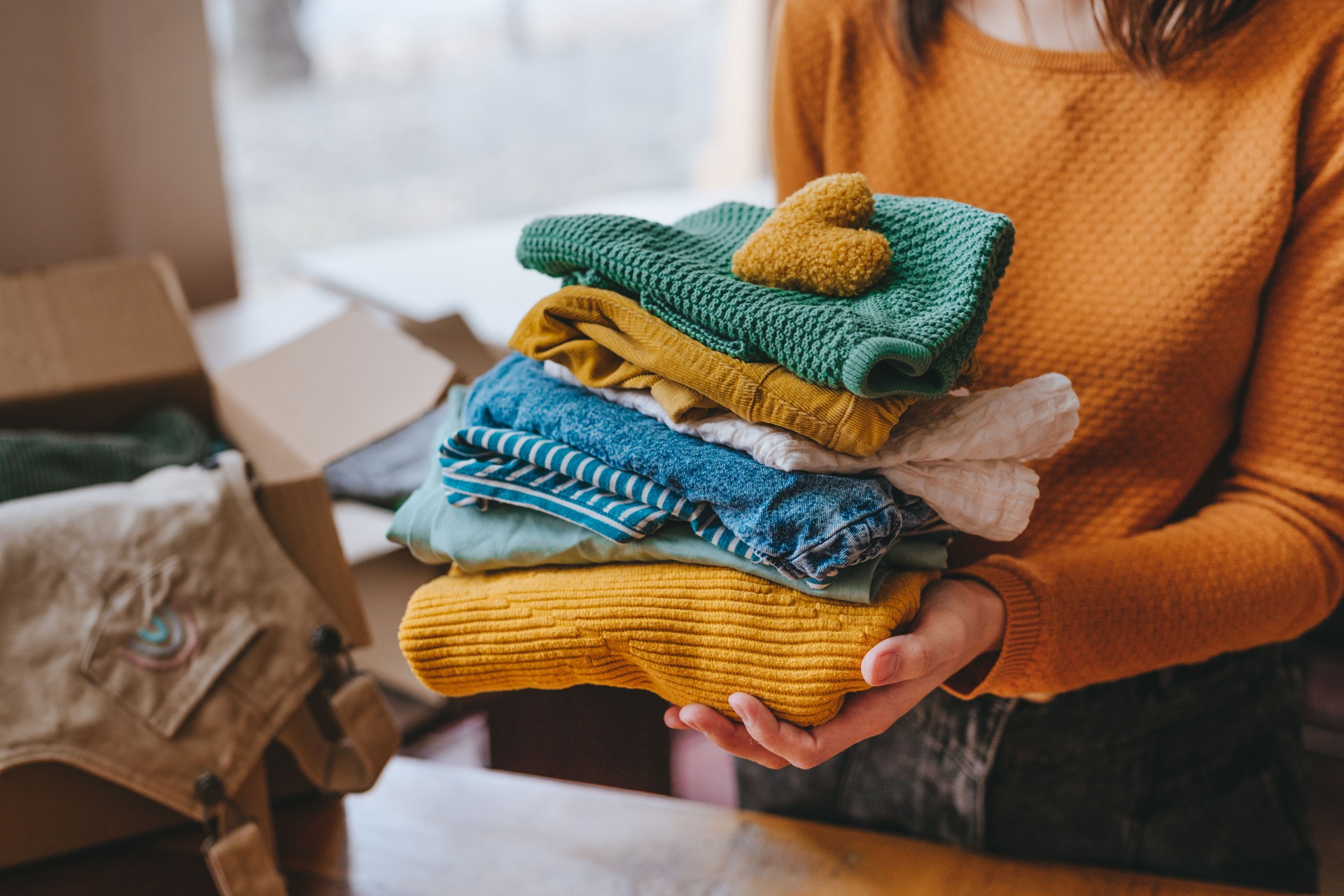 Close-up of female hands holding a fabric heart and clothes for charity