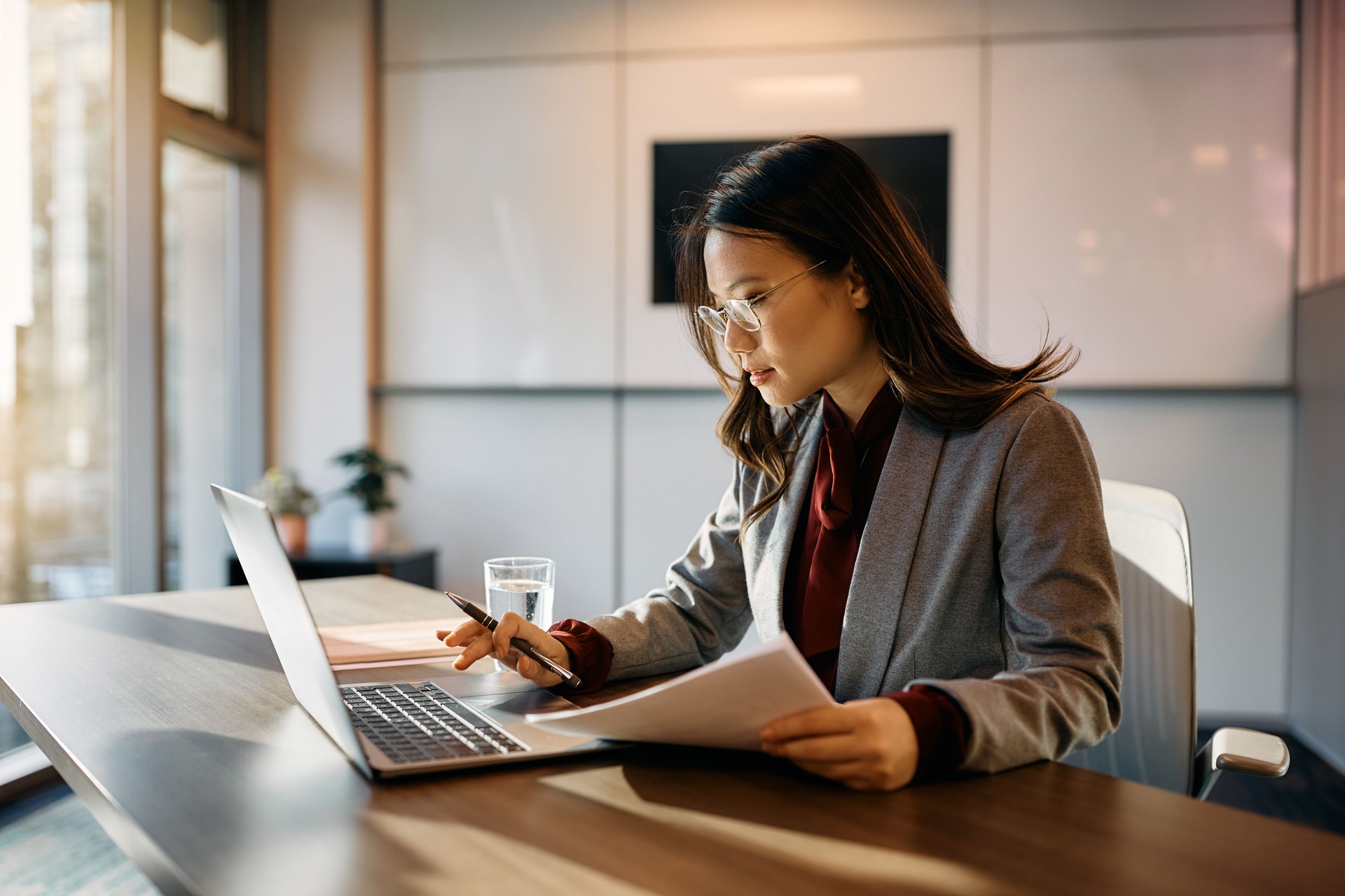 Asian businesswoman using laptop while analyzing reports in the office.