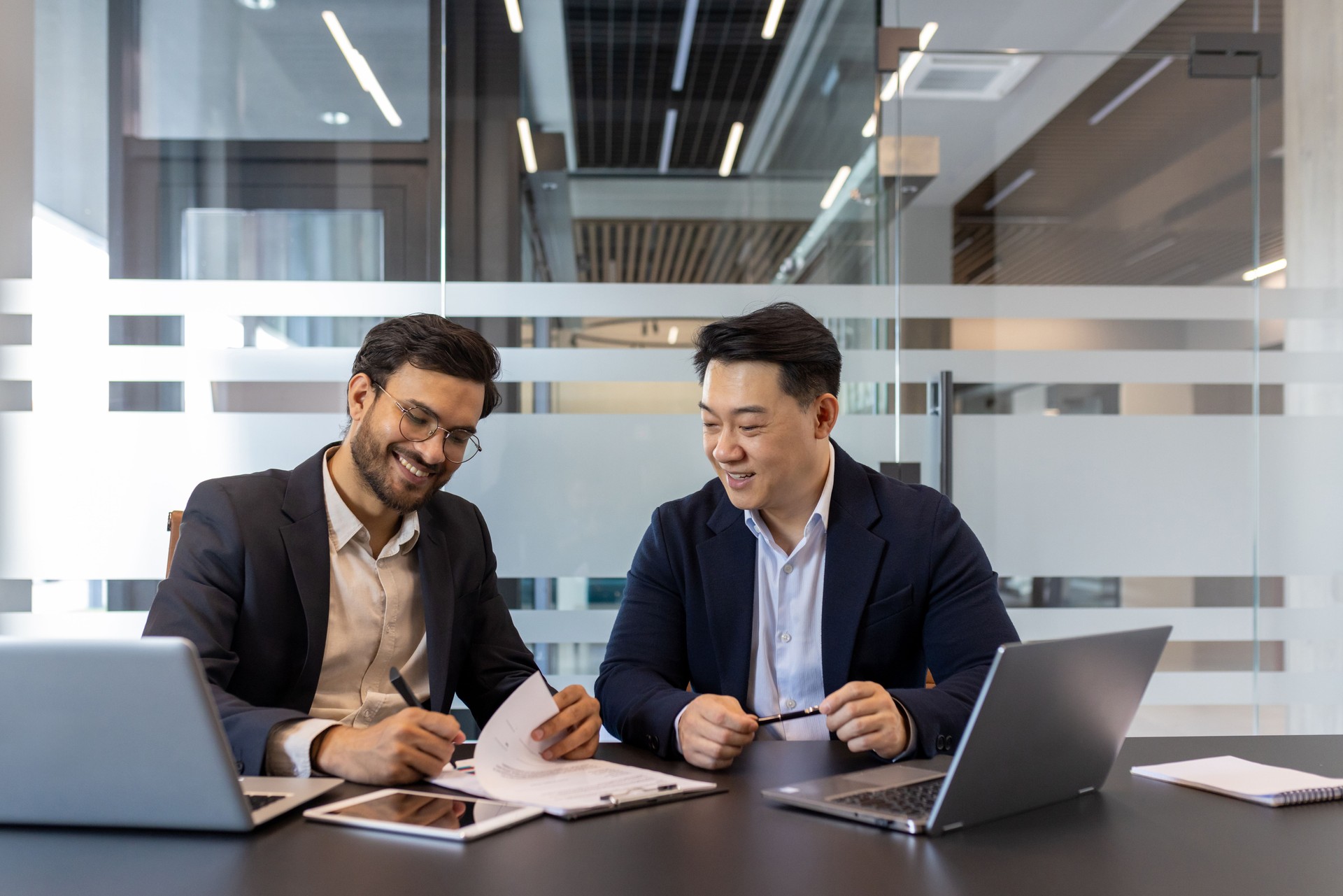 Two businessmen collaborating with documents and laptops in a modern office